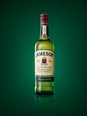 Jameson Irish whiskey bottle with red cap and green label on dark green background