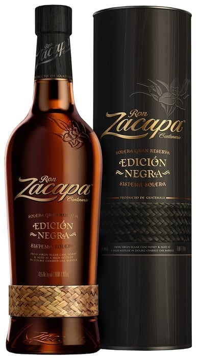Ron Zacapa Edición Negra rum bottle with straw wrap next to its black cylindrical packaging box